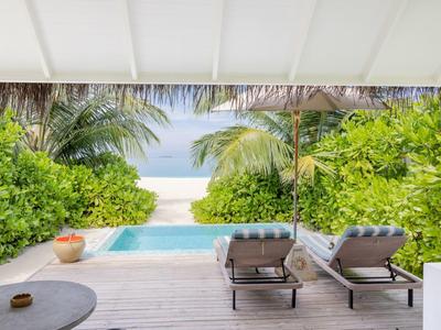 Blick von einer Terrasse mit Pool auf Strand und Meer, umgeben von Palmen und Grün.