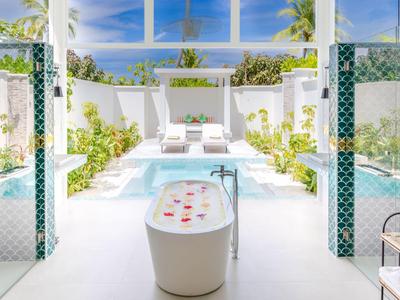 Helles Badezimmer mit freistehender Badewanne und Blick auf einen sonnigen Poolbereich.