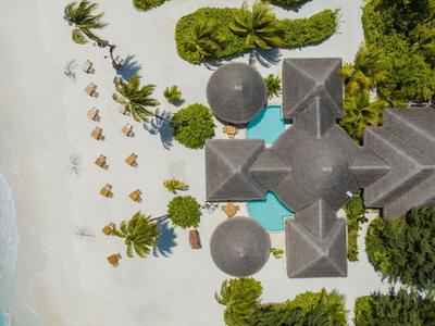 Vogelperspektive eines Resorts mit Pool, umgeben von Sandstrand und Palmen.