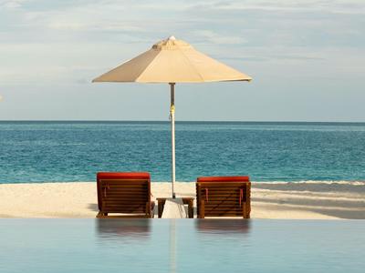 Zwei Liegestühle mit Sonnenschirm am Pool mit Blick auf das Meer.