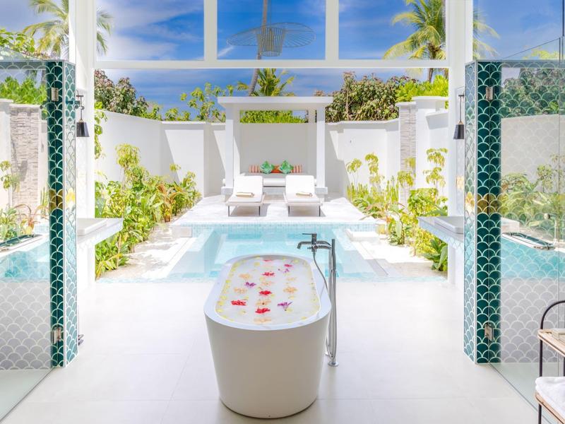 Helles Badezimmer mit freistehender Badewanne und Blick auf einen sonnigen Poolbereich.