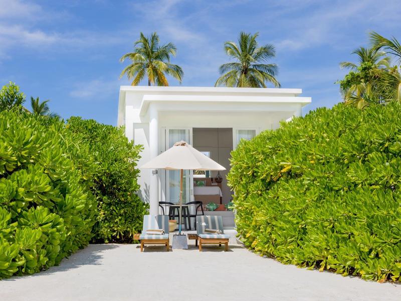 Modernes Ferienhaus am Strand mit Palmen und Liegestühlen.
