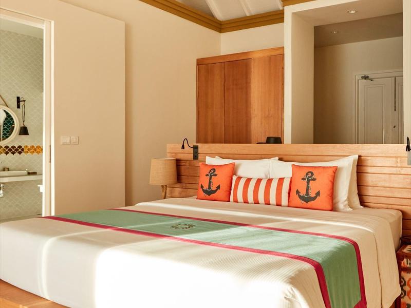 Hell eingerichtetes Schlafzimmer mit Holzmöbeln und maritimen Kissen auf dem Bett.