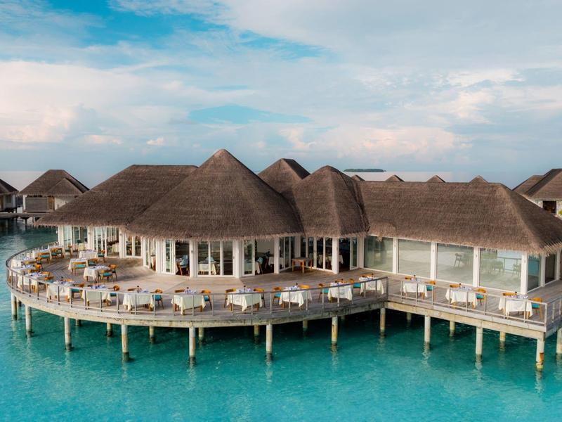 Luxuriöse Überwasserbungalows mit Strohdächern über klarem, türkisfarbenem Wasser.