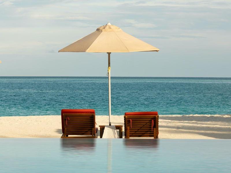 Zwei Liegestühle mit Sonnenschirm am Pool mit Blick auf das Meer.