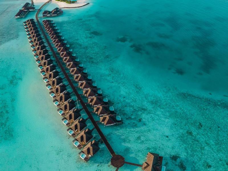 Luftaufnahme einer tropischen Insel mit Überwasser-Bungalows und klarem, türkisem Wasser.