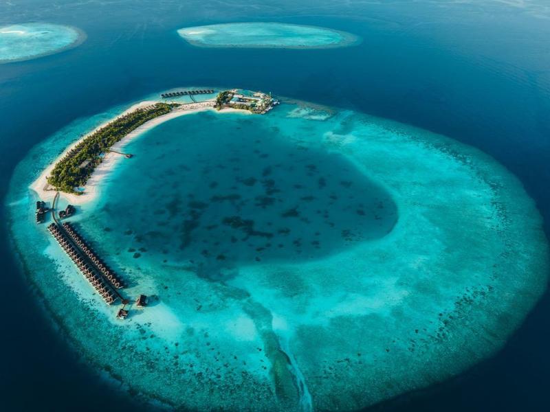 Luftaufnahme eines abgelegenen Inselresorts umgeben von türkisfarbenem Wasser und Korallenriffen.