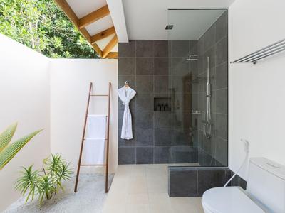 Modernes Bad mit begehbarer Dusche, weißer Badewand und Pflanzen neben der Holzleiter.