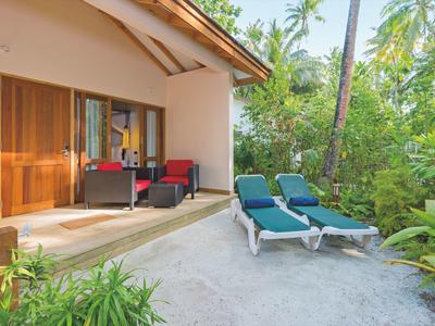 Zwei blaue Liegestühle vor einer Terrasse mit roten Sesseln in einem tropischen Garten.