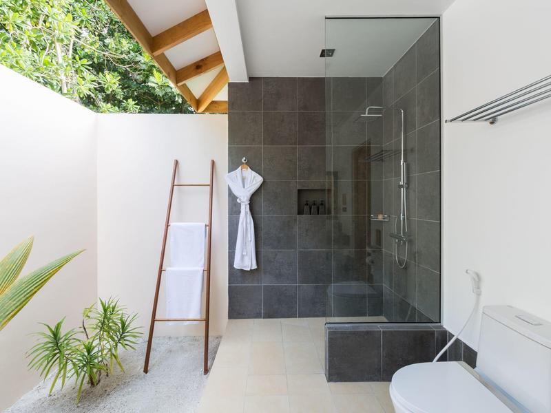 Modernes Bad mit begehbarer Dusche, weißer Badewand und Pflanzen neben der Holzleiter.