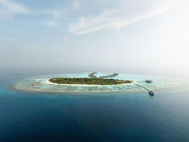 Pequeña isla tropical con vegetación verde, rodeada de aguas turquesas y un muelle.