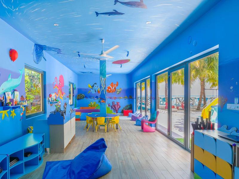 Sala de juegos infantil colorida con decoración submarina, pufs y grandes ventanas en el hotel.