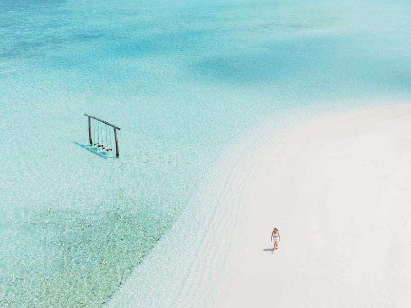 Playa con arena blanca y agua turquesa clara junto a bungalows sobre el mar.