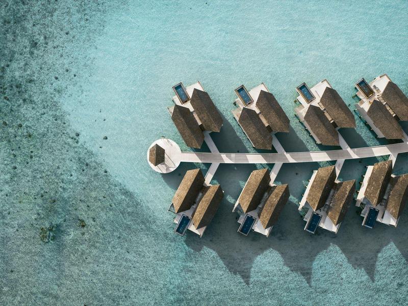 Bungalows sobre el agua en mar turquesa claro, vista aérea.