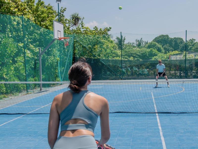 Mujer en cancha de baloncesto, vista trasera en día soleado con fondo verde.