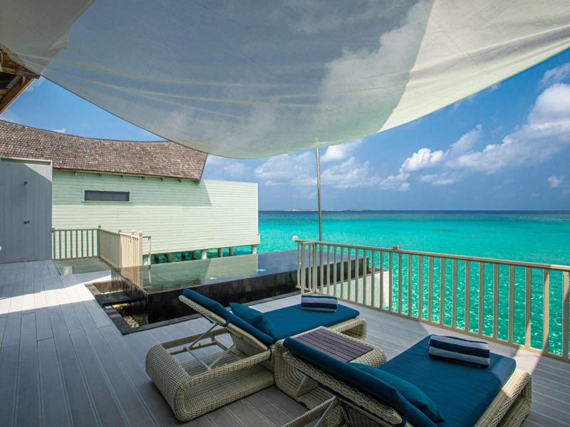 Balcón con tumbonas azules y vista al mar turquesa bajo un cielo azul.