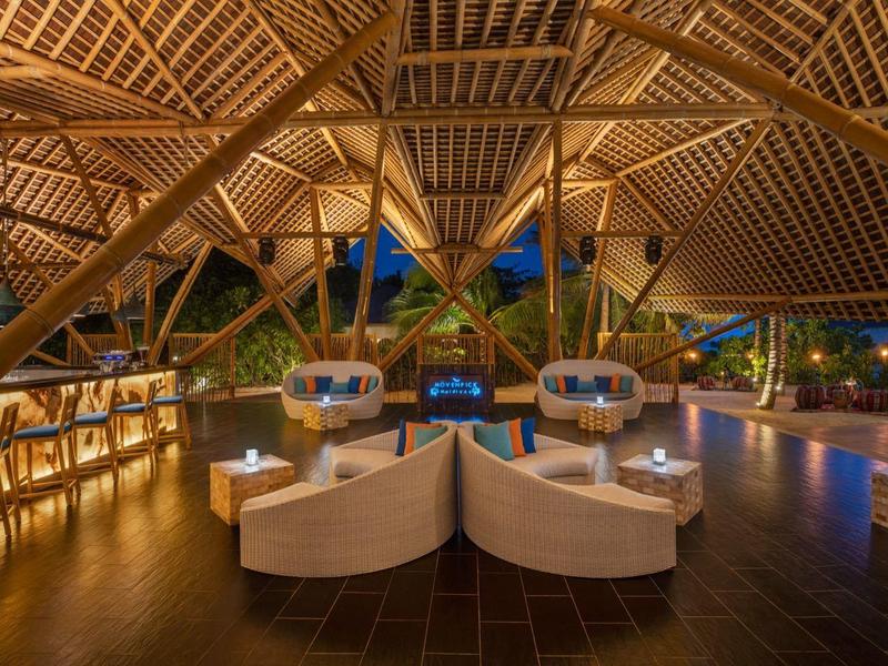 Área de salón abierta con techo de madera, sillas elegantes y iluminación ambiental nocturna.