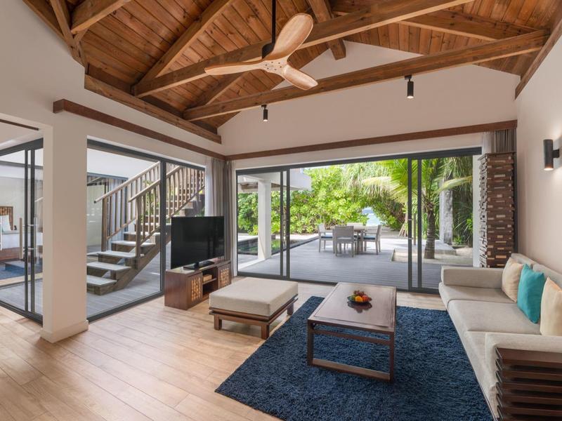 Sala de estar luminosa con techo de madera, grandes ventanas de vidrio y muebles modernos con sofá y televisor.