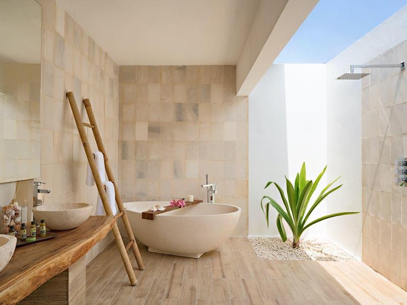 Baño luminoso con bañera independiente, escalera de madera y ducha abierta con planta verde.