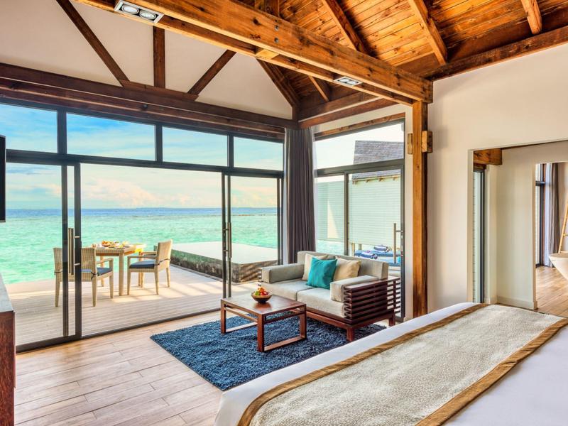 Habitación de hotel moderna con vista al mar, techo de madera y acceso a terraza con zona de estar junto al mar.