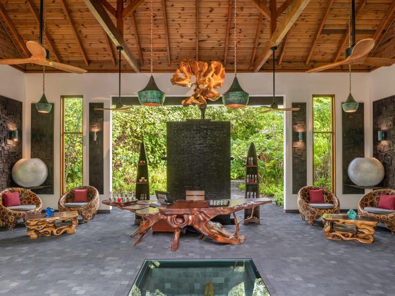 Lobby de hotel lujosa con techo de madera, muebles artísticos y grandes ventanales con vista al jardín.