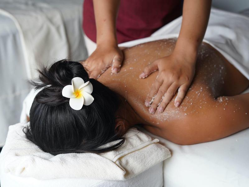 Mujer recibiendo masaje de espalda con flor en el cabello en un ambiente relajante de spa.
