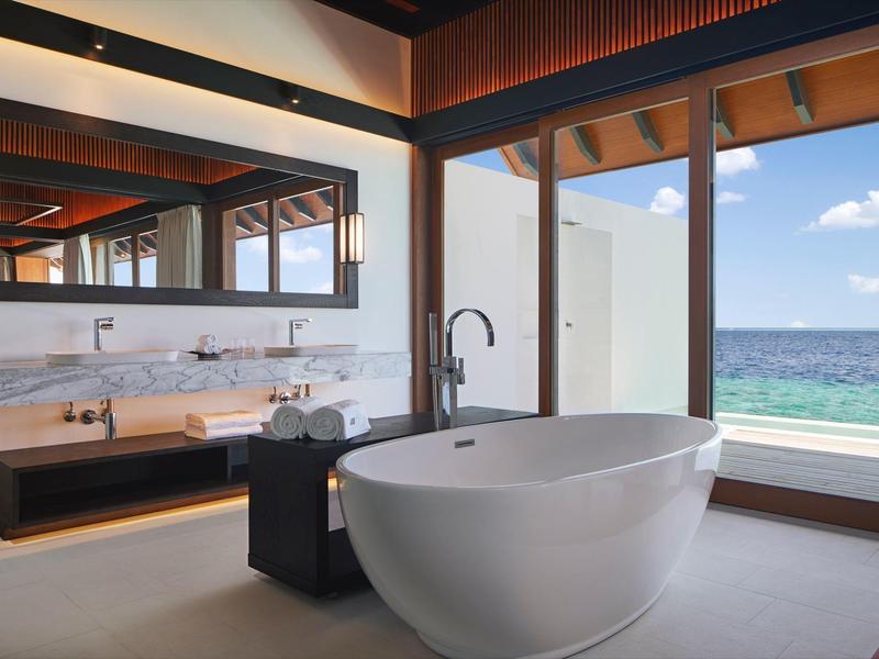 Modernes Badezimmer mit freistehender Badewanne, großem Spiegel und Meerblick durch große Fenster.