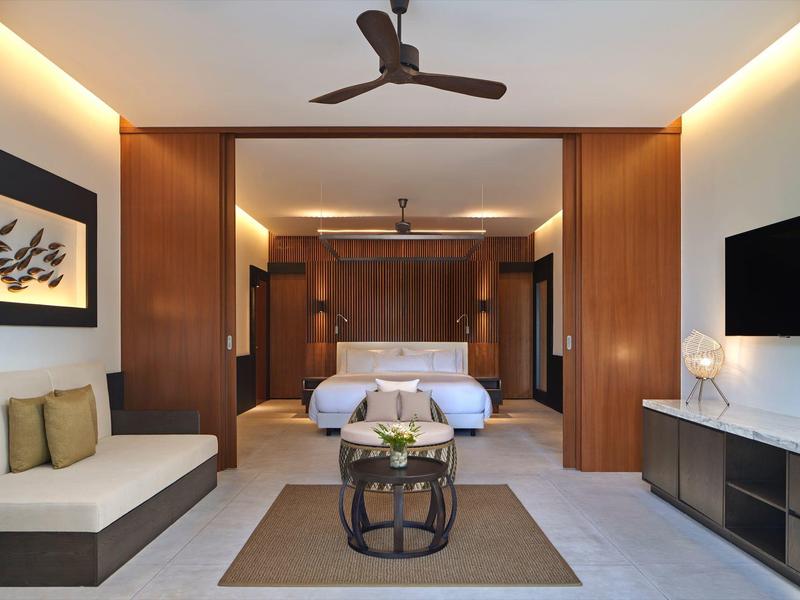 Modernes Hotelzimmer mit Holzakzenten, Doppelbett, Sofa, Deckenventilator und TV-Wand.