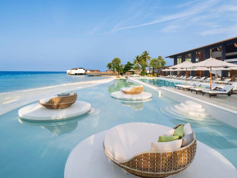 Luxuriöser Pool am Meer mit runden Korbsesseln und Liegestühlen bei klarem Himmel.