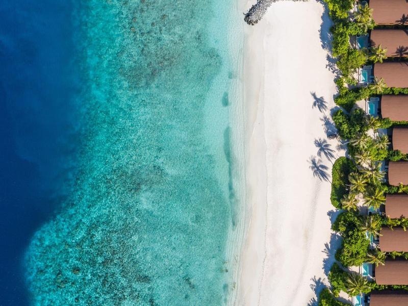 Weiße Sandstrände, blaues Meer, grüne Palmen und braune Strandbungalows in Reihen angeordnet.