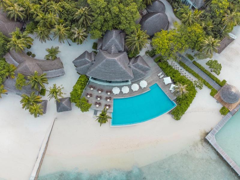 Vogelperspektive auf ein tropisches Resort mit Pool, umgeben von Palmen nahe am Strand.
