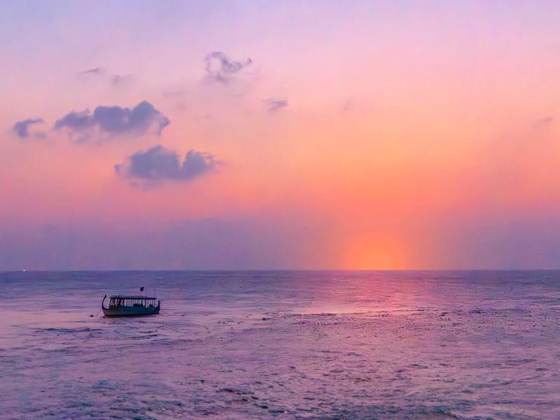 Ein Boot auf ruhigem Wasser bei Sonnenuntergang mit orange-purpurfarbenem Himmel.