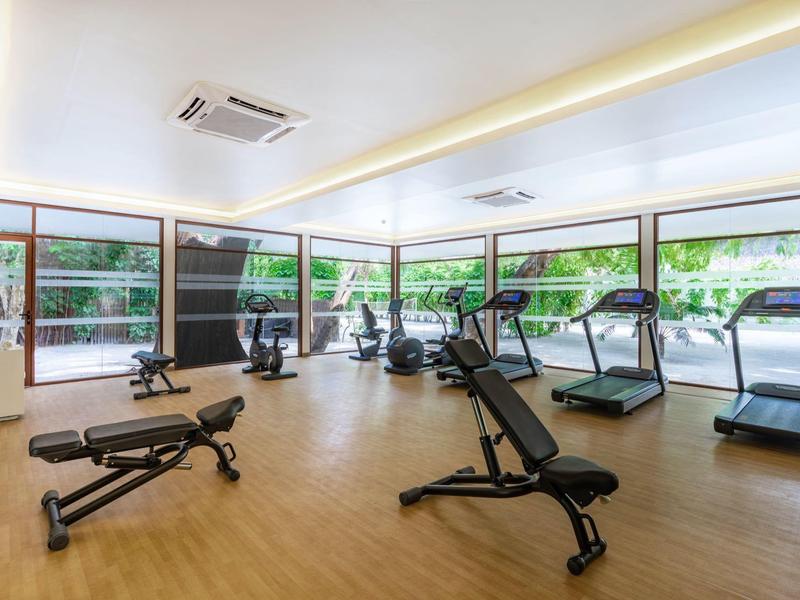 Heller Fitnessraum mit vielen Trainingsgeräten und großen Fenstern mit Blick ins Grüne.