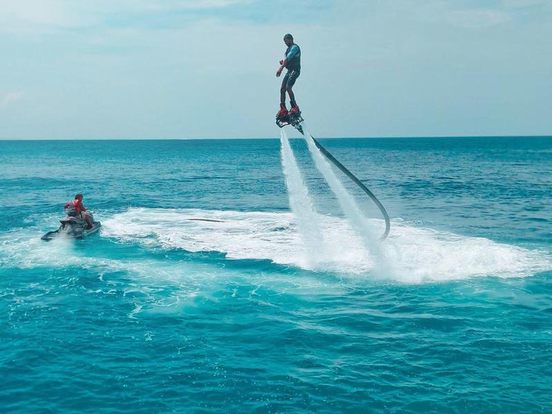 Person fliegt mit Flyboard über dem Meer, begleitet von Motorboot bei klarem Himmel.