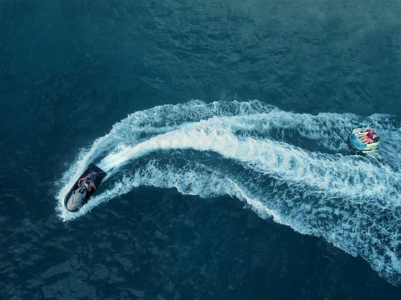 Ein schwarzes Jetboot zieht eine gelbe Banane auf dem blauen Wasser hinter sich her.