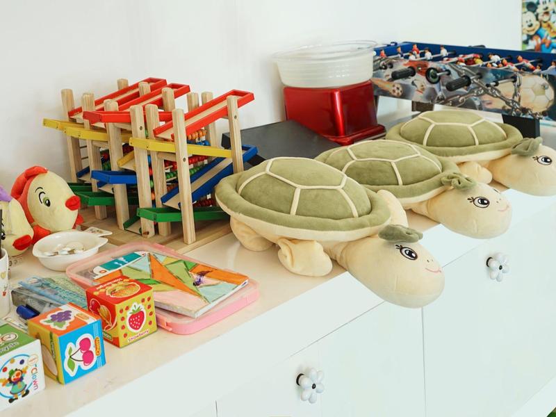 Weiße Kommode mit drei Plüschturtles und buntem Spielzeug darauf in einem hellen Raum.