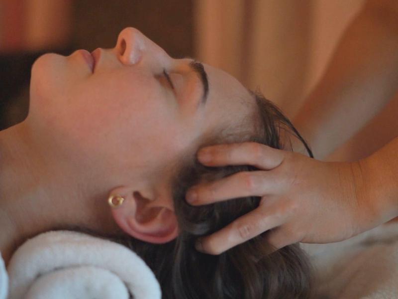 Frau liegt entspannt mit geschlossenen Augen, während Hände sanft ihren Kopf massieren.