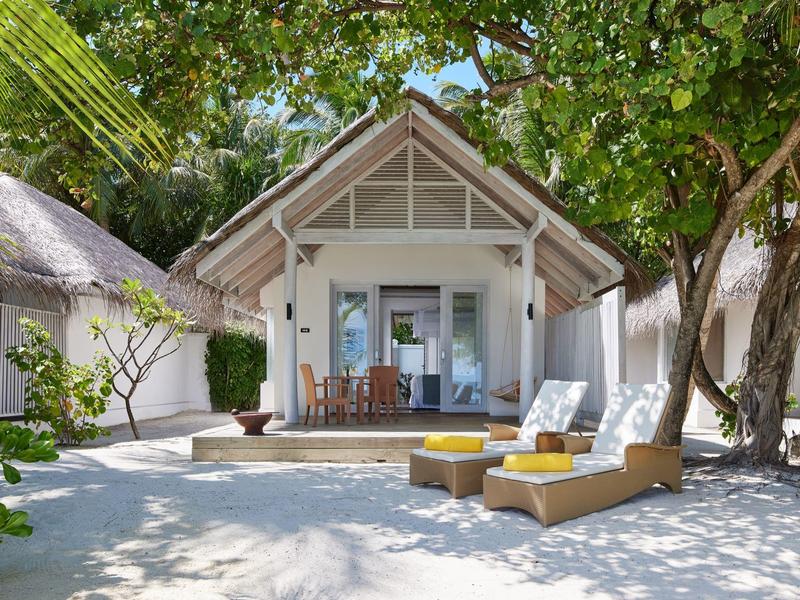 Strandbungalow mit Terrasse und Liegestühlen unter Bäumen