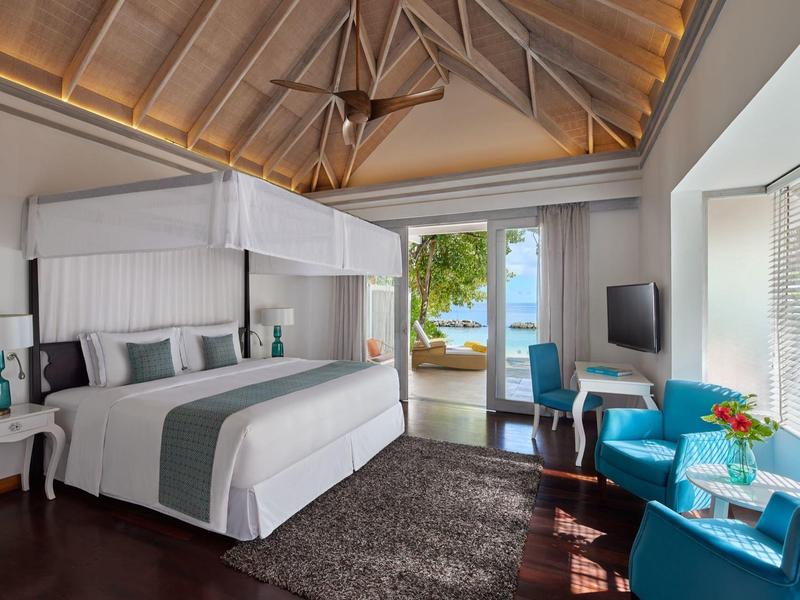 Luxuriöses Hotelzimmer mit Himmelbett, blauen Sesseln und Blick auf Terrasse mit Meer