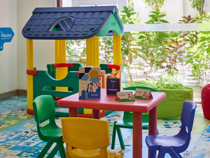 Bunter Kinderspielbereich mit kleinem Spielhaus und mehreren bunten Stühlen und Tischen.