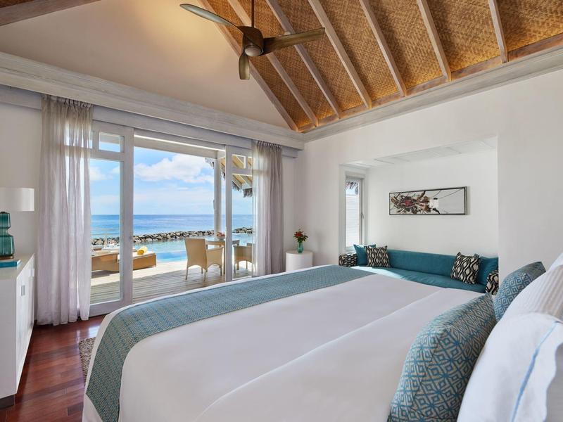 Helles Hotelzimmer mit großem Bett und Meerblick durch große Fenster.