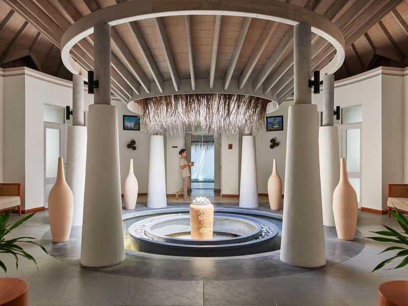 Moderner Hotellobby mit zentralem Brunnen, weißen Säulen und eleganter, runder Decke.