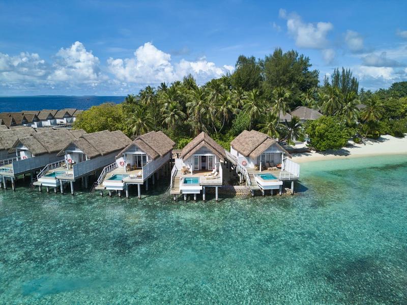 Reihen von Überwasserbungalows mit Terrassen über türkisfarbenem Meerwasser und weißem Sandstrand