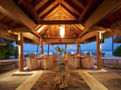 Area pranzo coperta all'aperto in stile rustico con vista sulla spiaggia al crepuscolo.