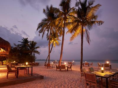 Scena serale di ristorante sulla spiaggia con tavoli sotto palme e vista mare.