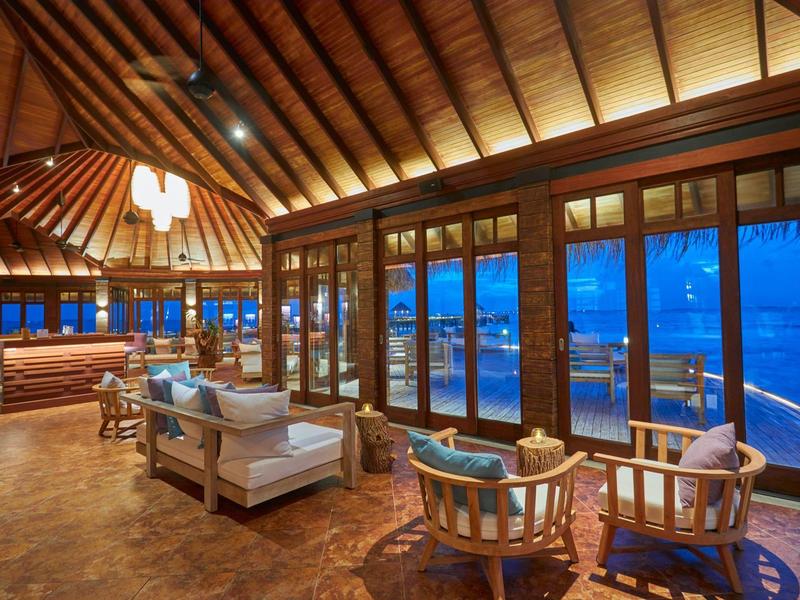 Großer Raum mit Holzboden und Dach, Glaswänden und bequemen Sesseln mit Meerblick.