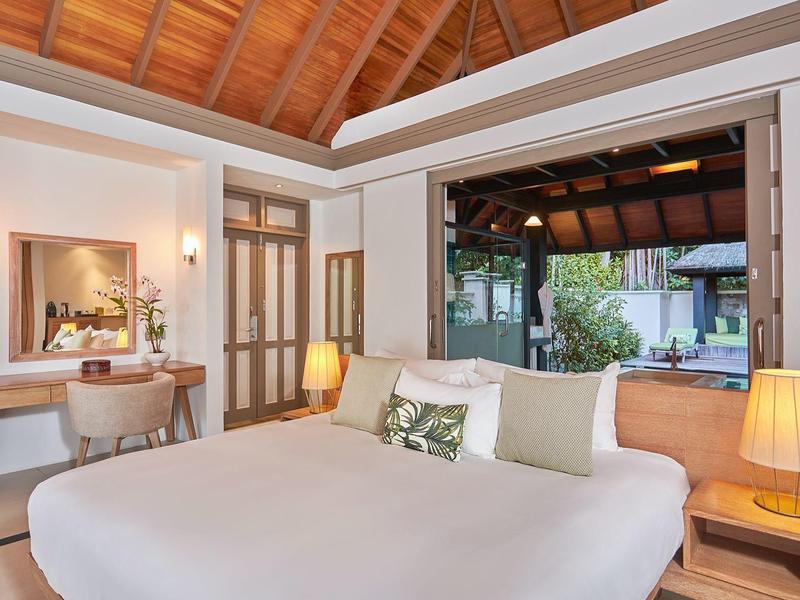 Helles Schlafzimmer mit Holzbett, großen Fenstern, Holzbalkendecke und Schreibtisch mit Stuhl.