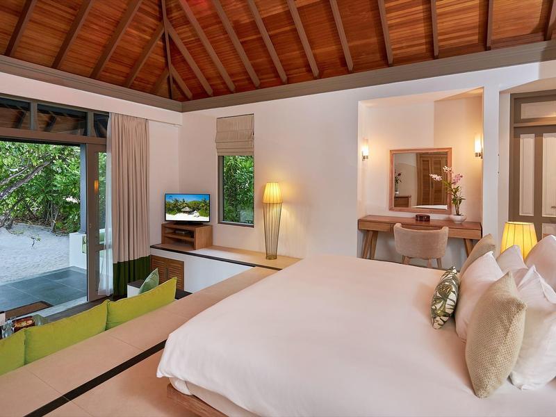 Schlafzimmer mit großem Bett, Holzdach, Lounge-Sofa und Blick auf Terrasse mit Garten.