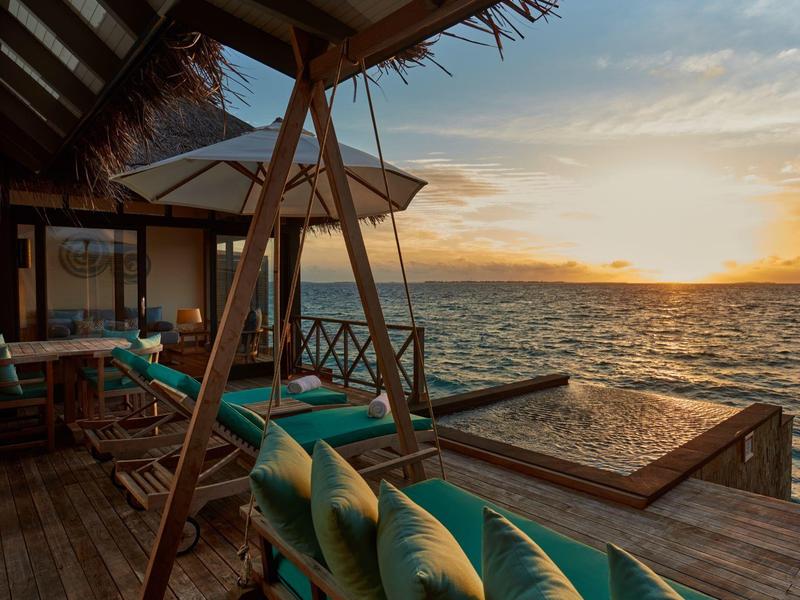 Holzterrasse mit Sitzbereich, Schaukel und Blick auf Meer bei Sonnenuntergang.