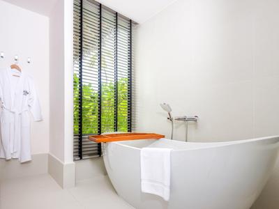 Helle Badezimmer mit freistehender weißer Badewanne, Handtuch, Holzablage und Fenster mit schwarzen Lamellen.